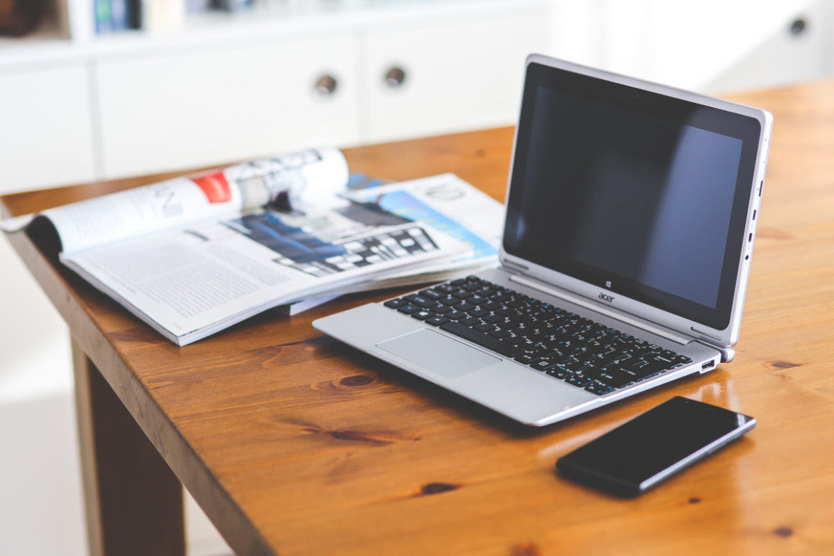 Acer Chromebook on a wooden desk next to an open magazine and smartphone, illustrating tips for sanitizing your device