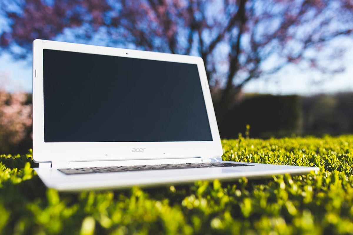 White laptop on grass with blurred trees in the background, symbolizing the eco-friendly benefits of refurbished electronics
