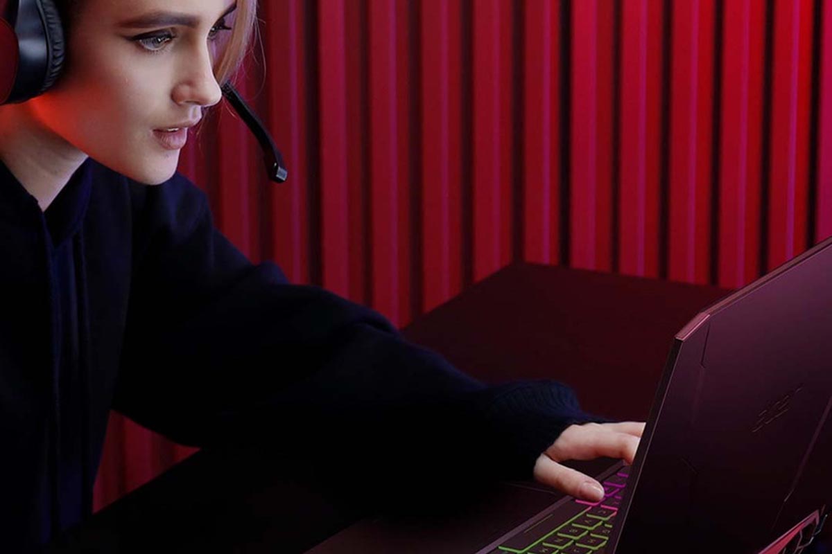 Gamer wearing a headset using a laptop in front of a red curtain, representing the value of recertified gaming devices