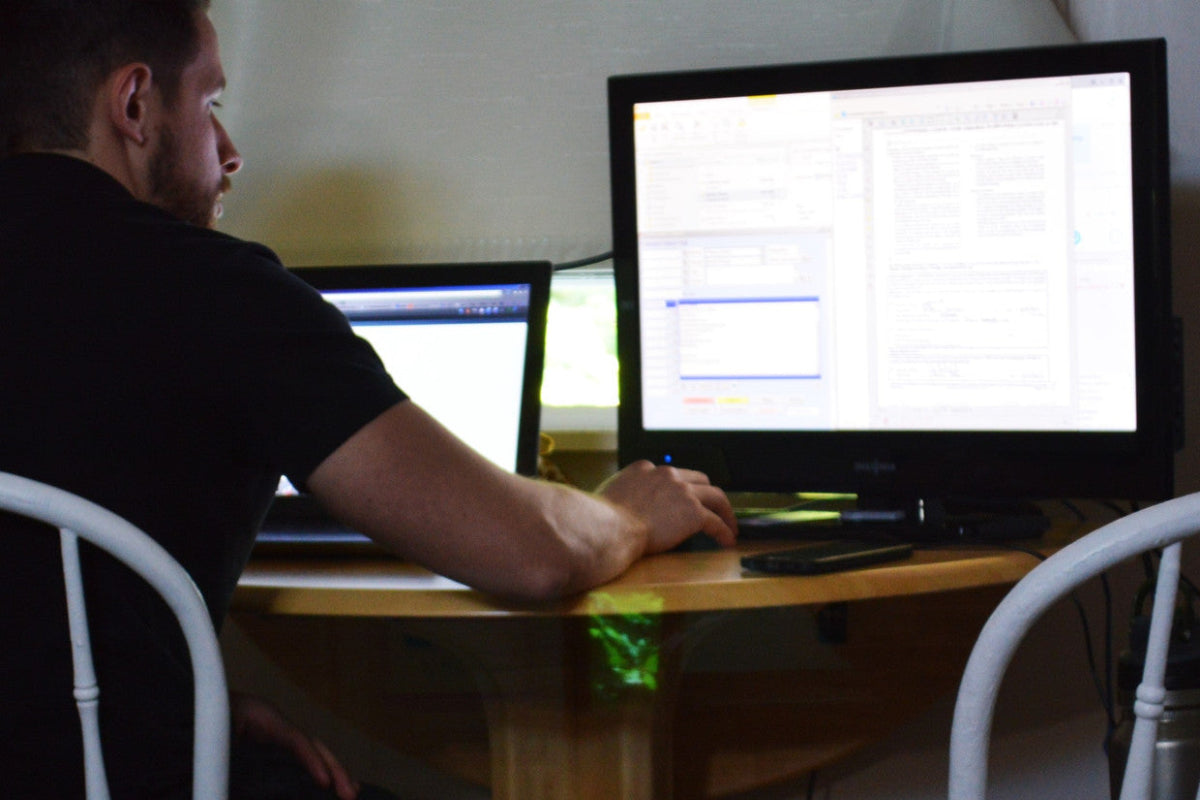 Person working at a desk with an Acer refurbished computer monitor and laptop in a dimly lit room