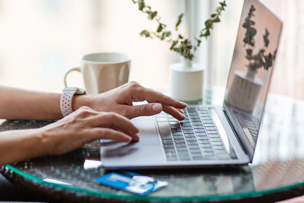 Person typing on a laptop with a coffee mug and plant nearby, illustrating a guide to buying refurbished laptops